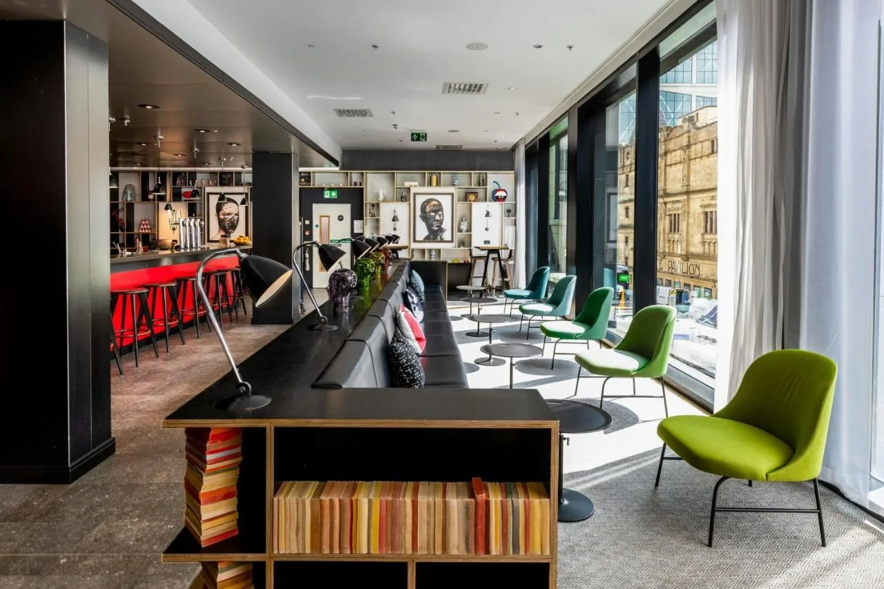 a waiting room with green chairs and a library at citizenM Glasgow in Glasgow